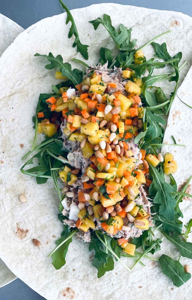 Image of a wheat wrap topped with some rocket salad, corn, red onions, and yellow paprika